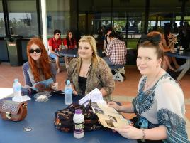 PhotoID:11951, Mackay O Week L-R Emma Lynch, Natalie Westcott, Deneal Ronald reading Be Magazine